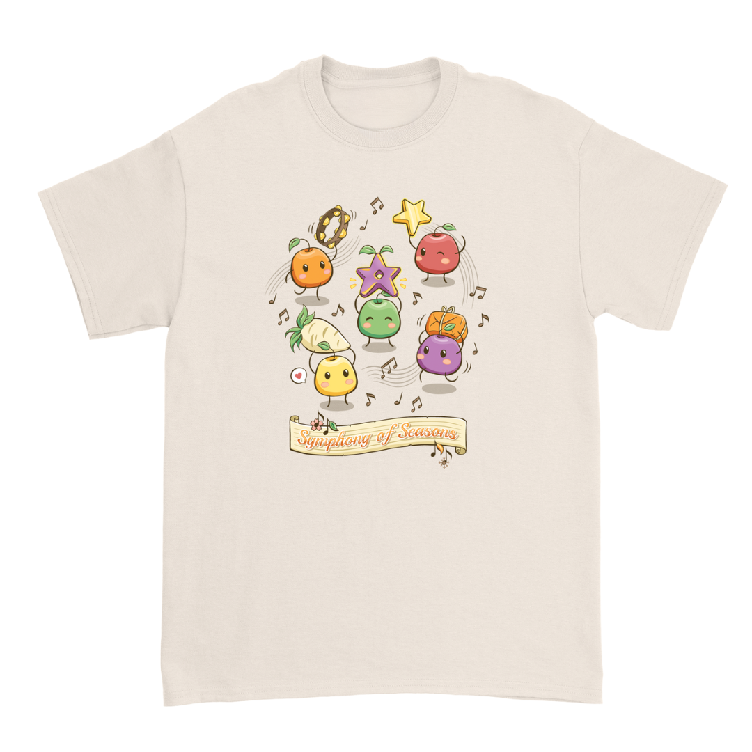 Cream-colored cotton t-shirt featuring a playful, colorful illustration of anthropomorphic fruits and vegetables dancing with musical notes above the text ’symphony of seasons.’